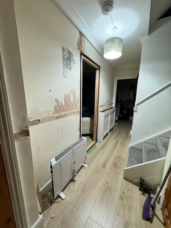 Residential hallway mid-renovation with stripped walls, before refurbishment works